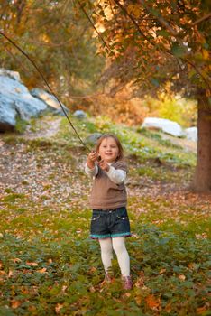 Small girl (3 years old) with smile in casual clothes plays with trees in autumn park.