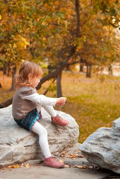 Small girl (3 years) tying shoelace in autumn park. Space for text