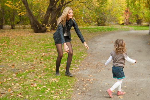 Family is playing in city park. Mother is trying to touch or catch small and fast girl (3 years old)