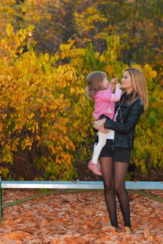 Mother hold her daughter in arms. Girl shows autumn leaf to her mother