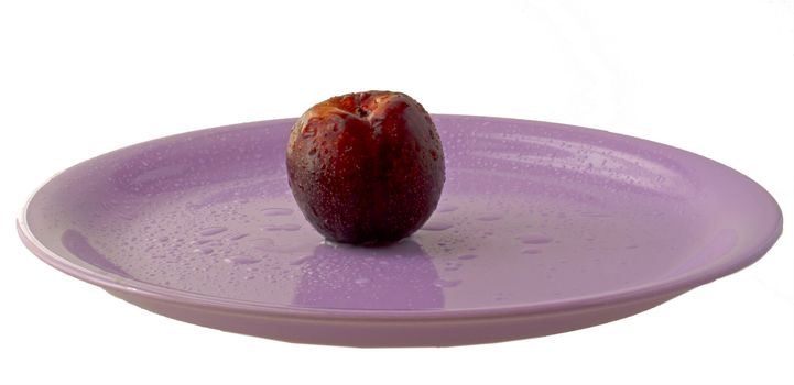 Lonely red plum over a violet plate, isolated over white