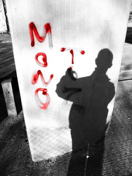 Vandal at work spraying graffiti on a pillar.