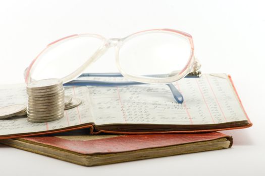 two financial ledgers with a pair of spectacles and a pile of coins on a white background