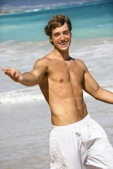 Attractive man walking on Maui, Hawaii beach smiling and reaching out.