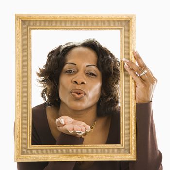 Woman holding frame around head blowing out kiss.