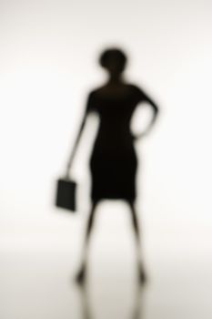 Soft focus silhouette of businesswoman standing with hand on hip holding briefcase.