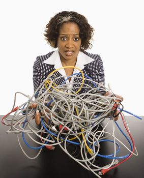 Businesswoman holding bundle of tangled computer cords with overwhelmed look on her face.