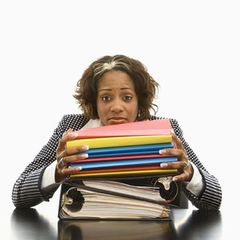 Businesswoman resting head on large stack of books and files looking overwhelmed.