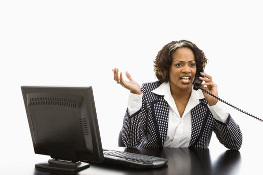 Businesswoman sitting at office desk with computer talking on telephone looking upset.