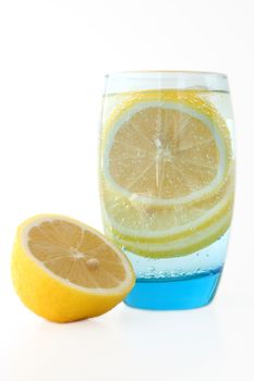 Lemon in glass with mineral water and ice.