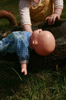 baby soaking a doll in an outdoor tub.