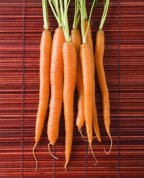 Close up of orange carrots with green tops against bamboo mat.