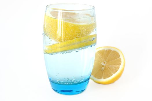 Lemon in glass with mineral water and ice.