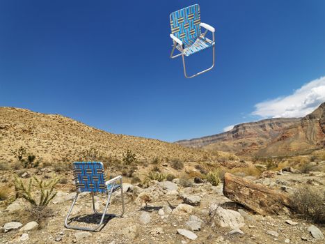 One lawn chair on ground and other up in the air in desert landscape.