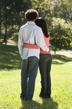 Rear view of couple standing in park with arms around eachother.
