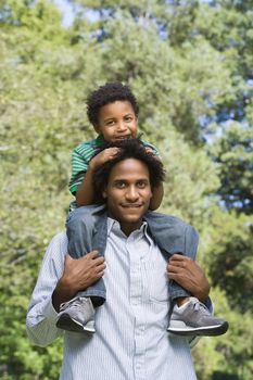 Father carrying son on shoulders in park.