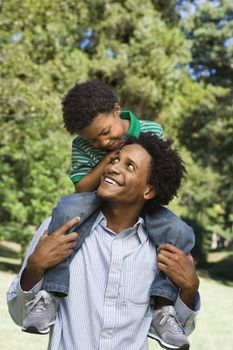 Father carrying son on shoulders in park.