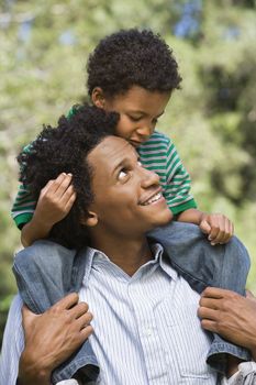 Father carrying son on shoulders in park.