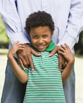 Smiling boy standing in front of father with his hands on shoulders.