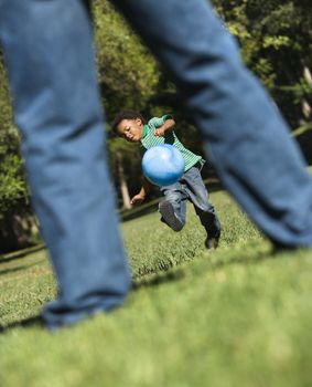 Son running and kicking ball towards father in park.