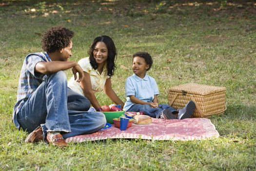 Smiling happy parents and son having picnic in park.