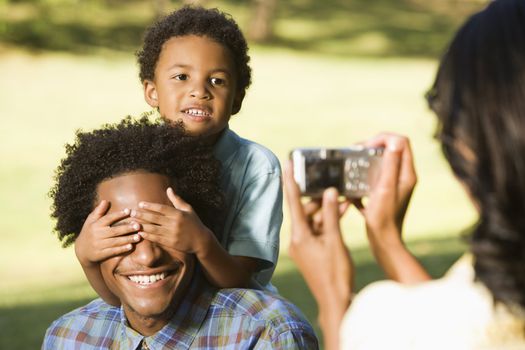 Woman photographing husband and son in park with digital camera.
