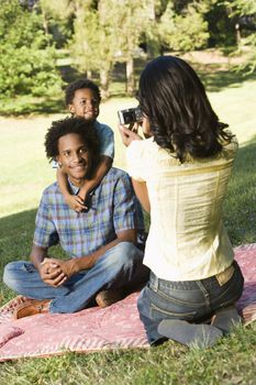 Mother photographing son and husband with digital camera in park.