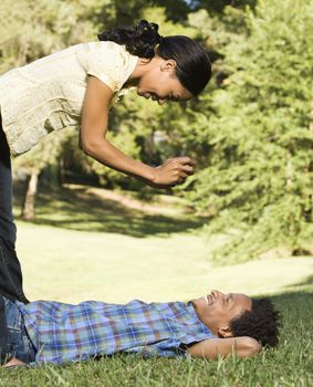 Woman standing over smiling man lying in grass taking his photograph.