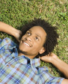 Portrait of man lying in grass smiling with hands behind head.