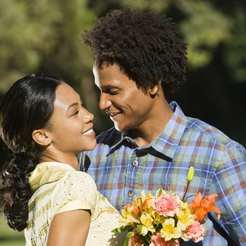 Woman holding flower bouquet and embracing man as they smile at eachother.