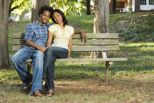 Happy smiling couple sitting on park bench together.