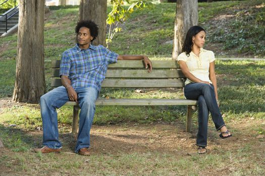 Man and woman sitting on opposite sides of park bench looking away from eachother.