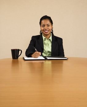 Businesswoman sitting at conference table smiling and writing in notebook.