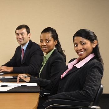 Businesspeople sitting at conference table smiling.