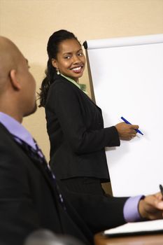 Businesspeople sitting at conference table while businesswoman gives presentation.