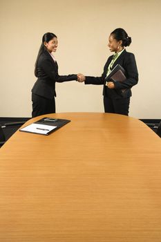Two businesswomen in suits shaking hands and smiling.