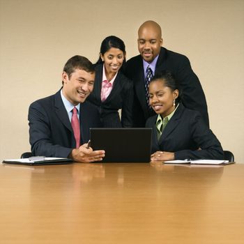 Businesspeople gathered around laptop computer looking at monitor and smiling.
