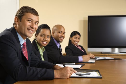 Businesspeople sitting at conference table smiling with flat screen display in background.