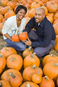 Couple picking out pumpkins and smiling at outdoor market.