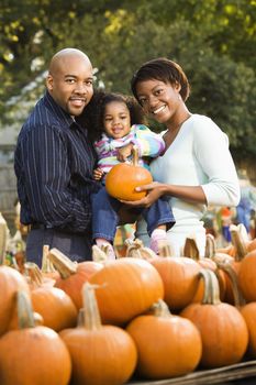 Parents and daughter picking out pumpkin and smiling at outdoor market.