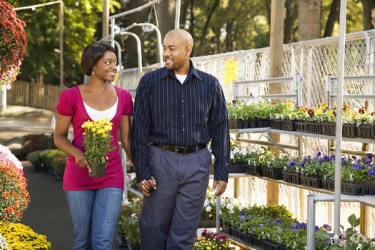 Happy smiling couple picking out flowers at outdoor plant market walking and holding hands.