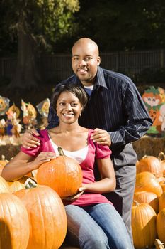 Portrait of happy smiling couple sitting in pumpkins at outdoor market.