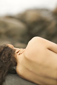 Rear view close up of young Caucasian woman lying nude on rock.