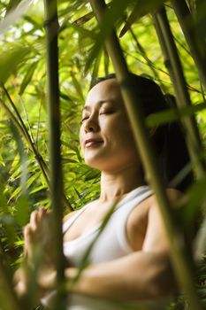 Portrait of Asian American woman in fitness attire standing in yoga position with eyes closed in bamboo forest in Maui, Hawaii.