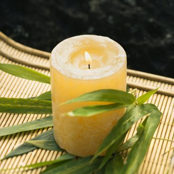 Burning candle on bamboo mat with bamboo leaves.
