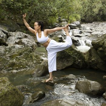 Asian American woman doing yoga balancing on boulder by creek in Maui, Hawaii.