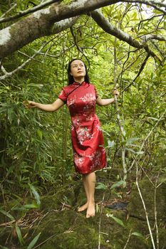 Portrait of Asian American woman in ethnic attire standing on rock in bamboo in Maui, Hawaii.