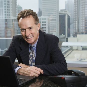 Middle-aged Caucasian male in office with skyline in background.