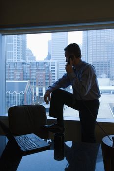 Middle-aged Caucasian male in office on phone with skyline in background.