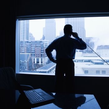 Middle-aged Caucasian male on phone in office with skyline in background.